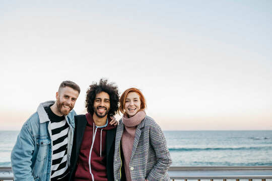 Three friends laughing together on a seafront promenade